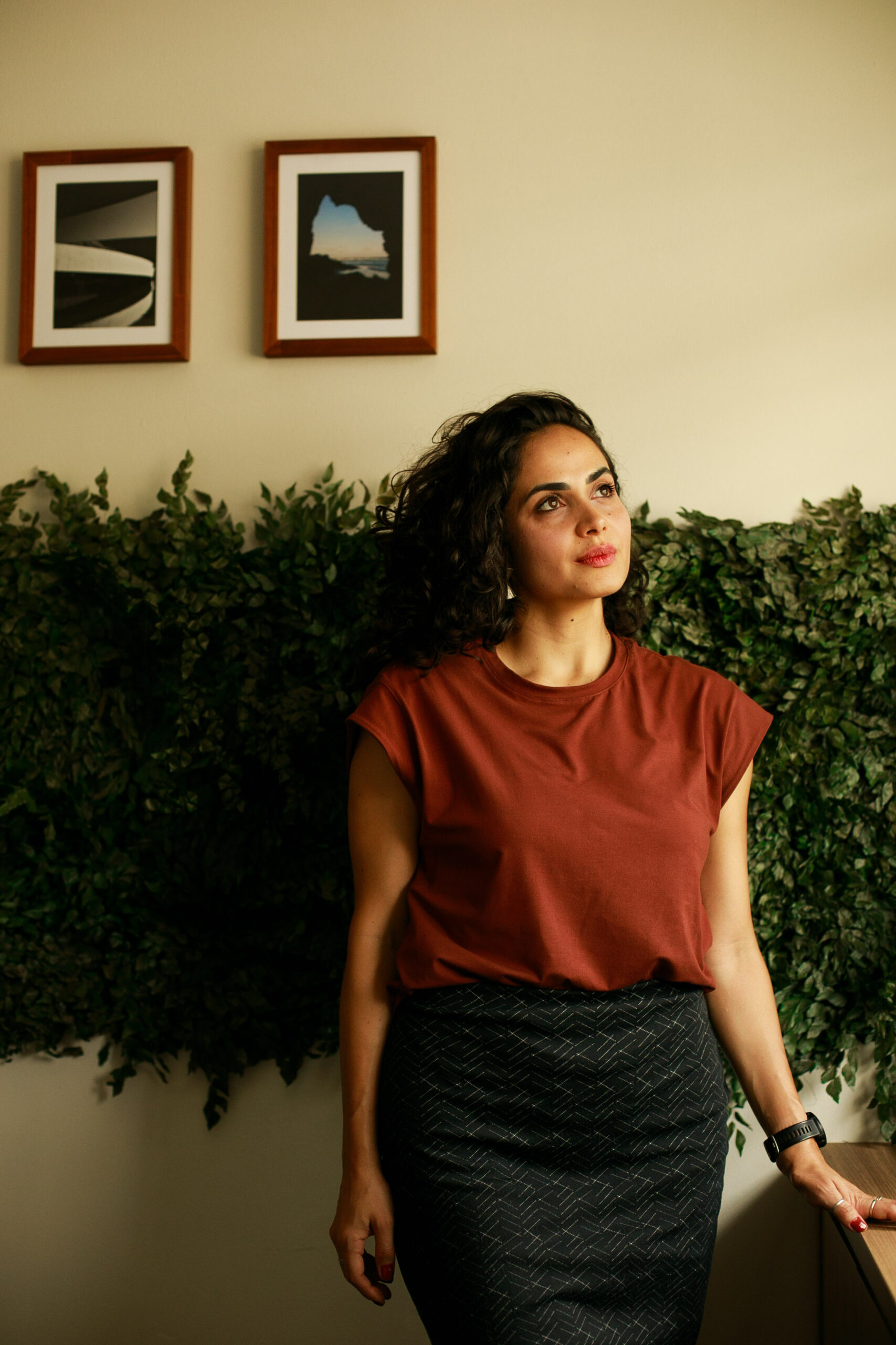 Arquiteta Mariane Borges no escritório da Revo, diante de uma parede com plantas e quadros
