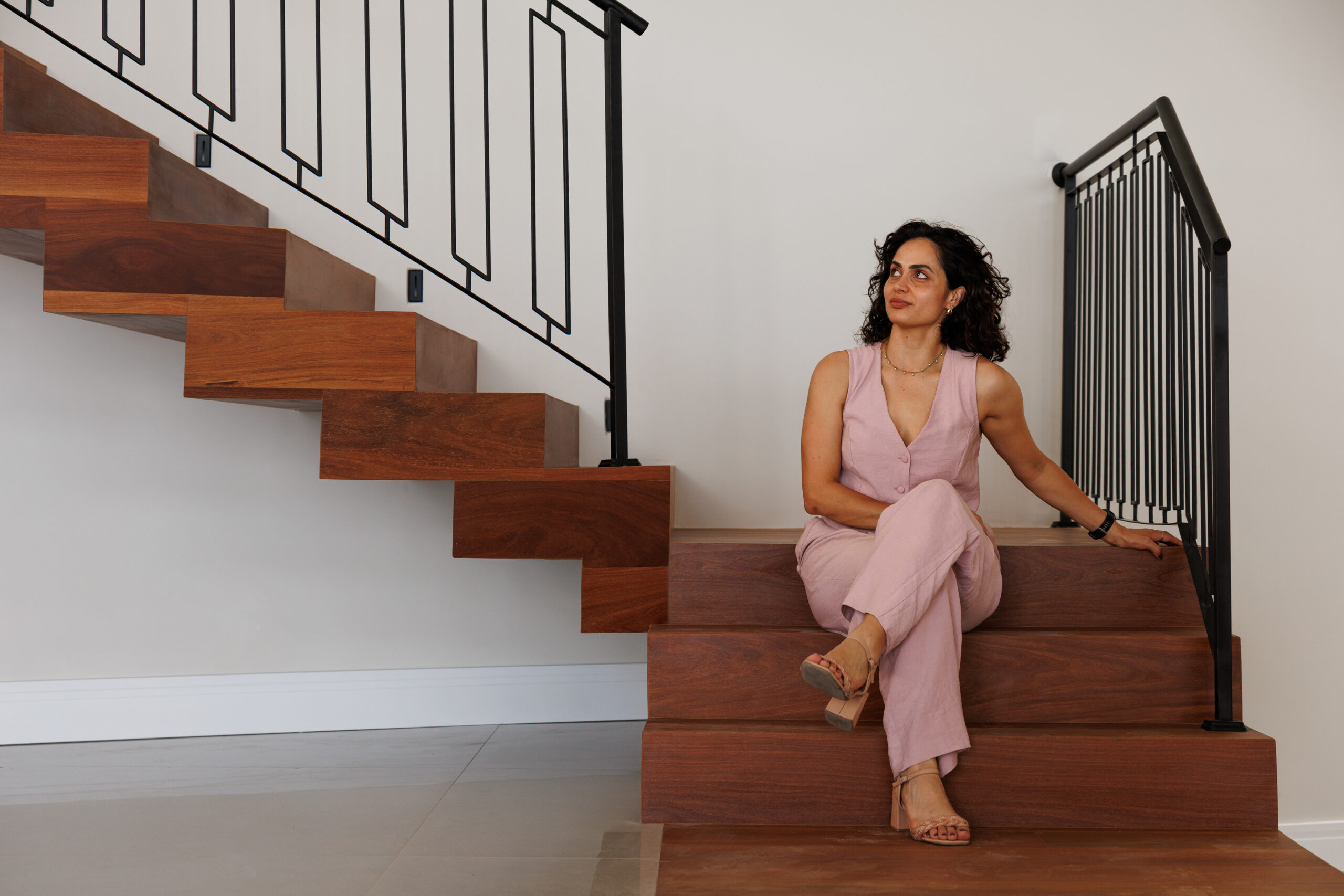 Mariane Borges, arquiteta da Revo, sentada na escada de madeira da Casa Tanguá